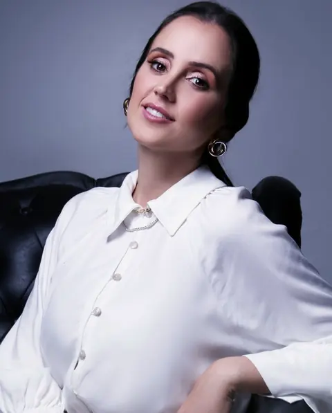 Dra. Deise Ferreira sentada numa poltrona, de camisa branca